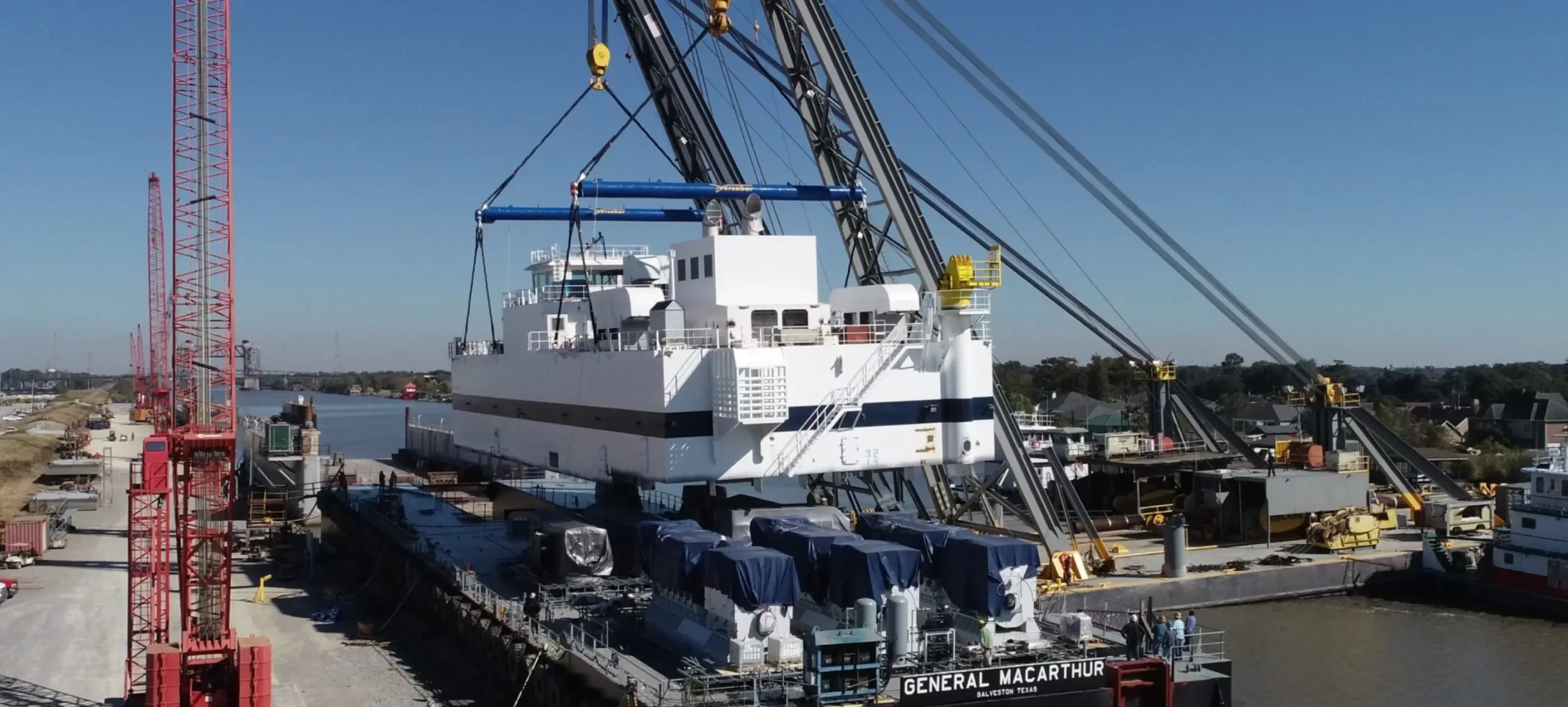 Large ship section being lifted by cranes at a busy shipyard dock.