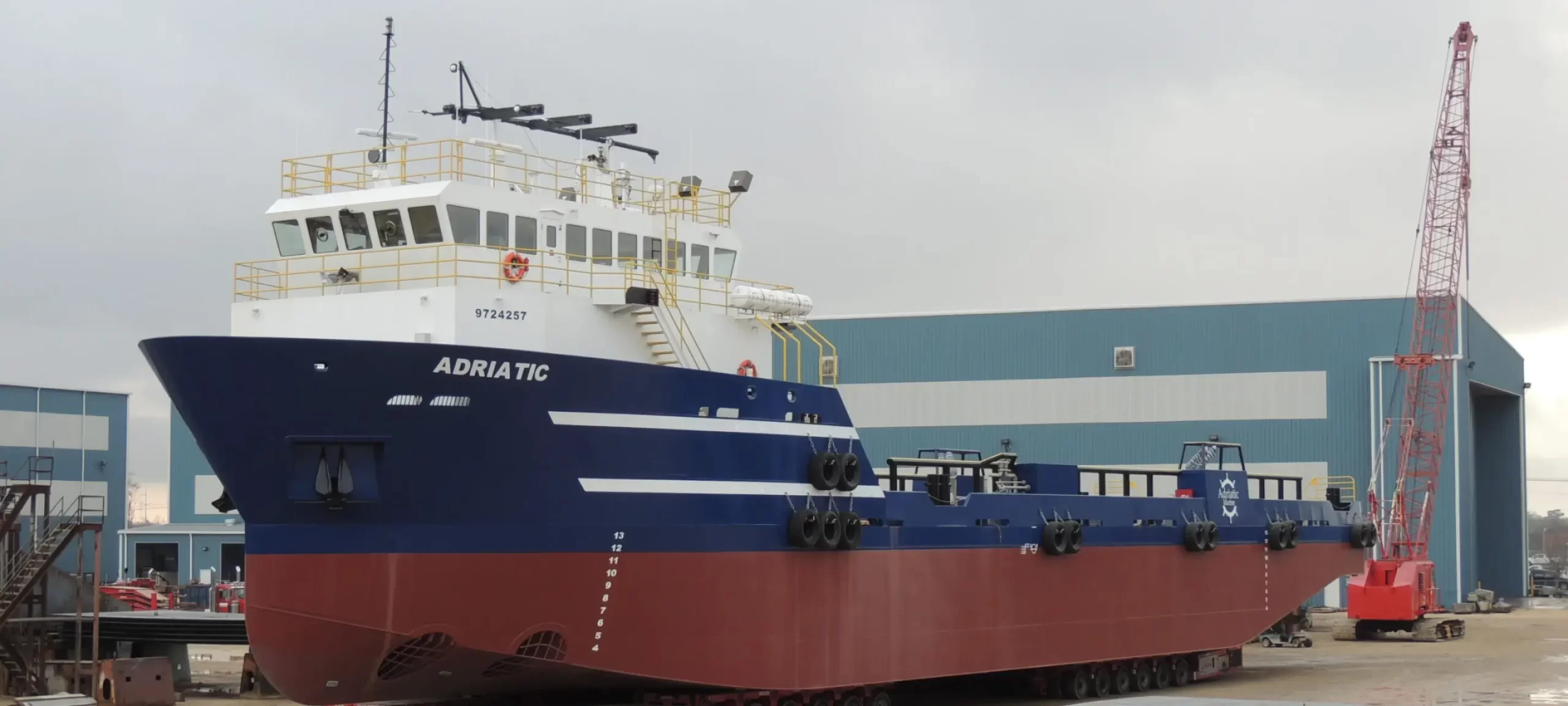 A cargo ship named Adriatic in a shipyard with industrial buildings and a crane in the background.