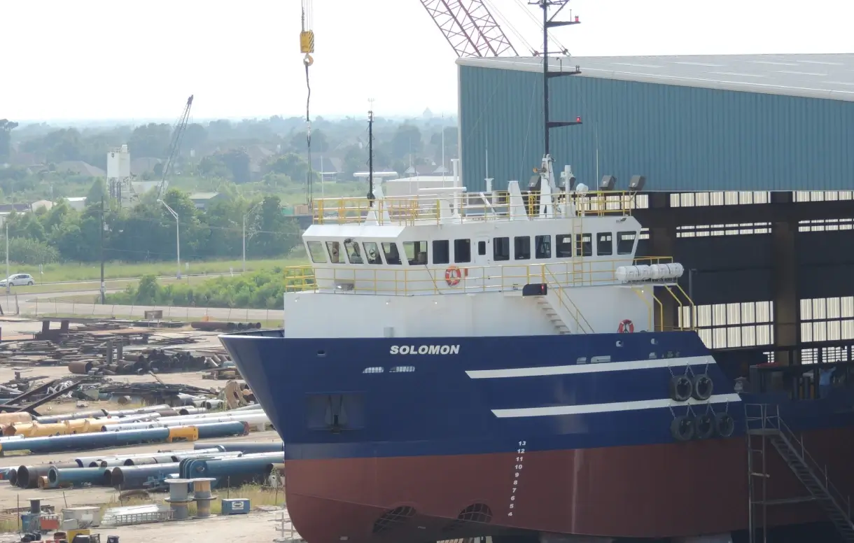 Offshore support vessel Adriatic alongside a shipyard building with cranes in the background.