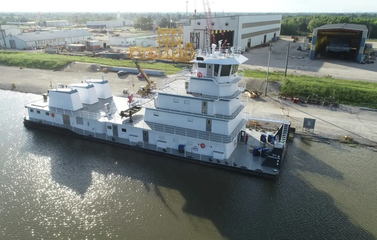 A large workboat docked at a shipyard along a river.